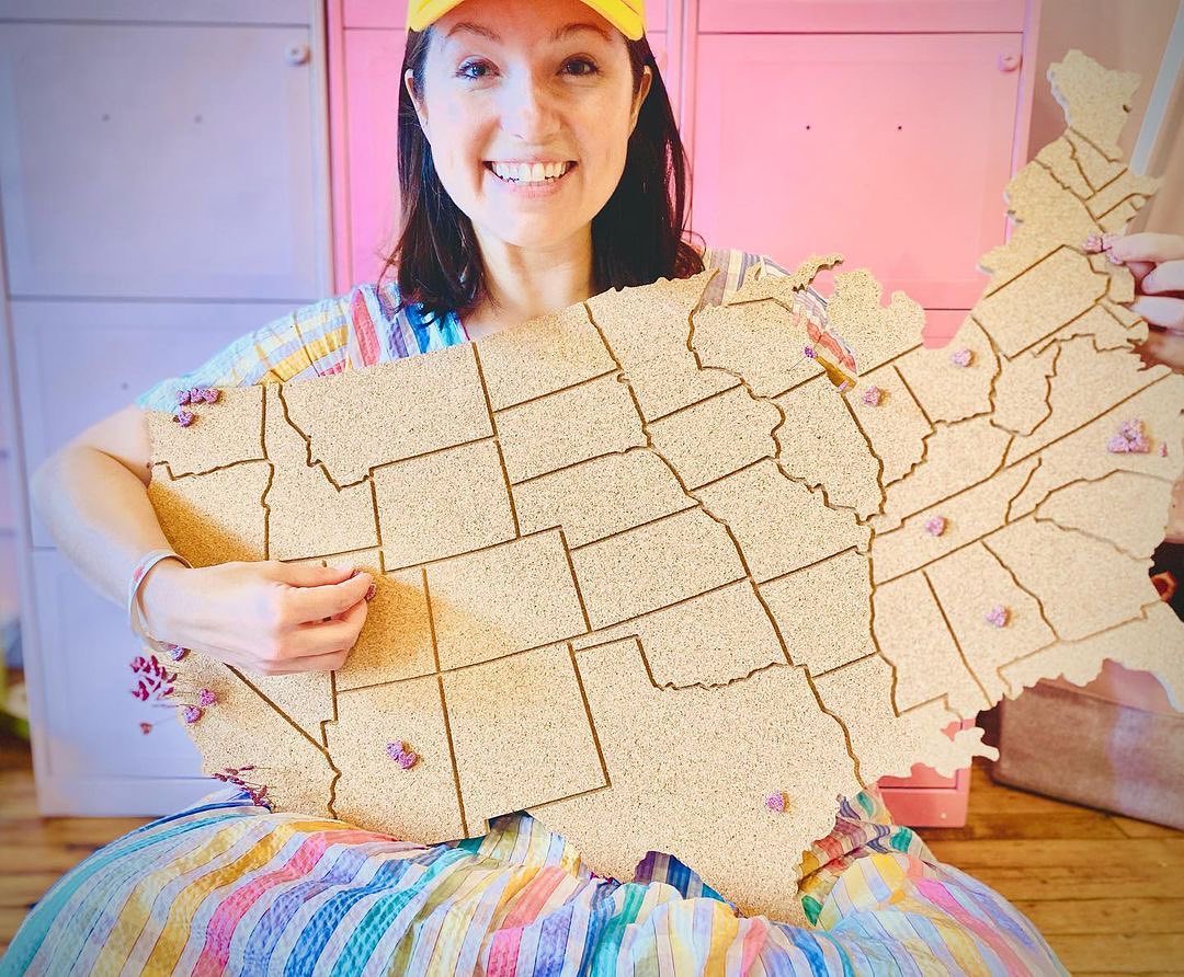 Genevieve Weeks holds a corkboard map of the USA with locations pinned.