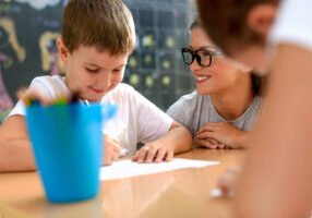 Preschool teacher looking at smart smiling boy at kindergarten