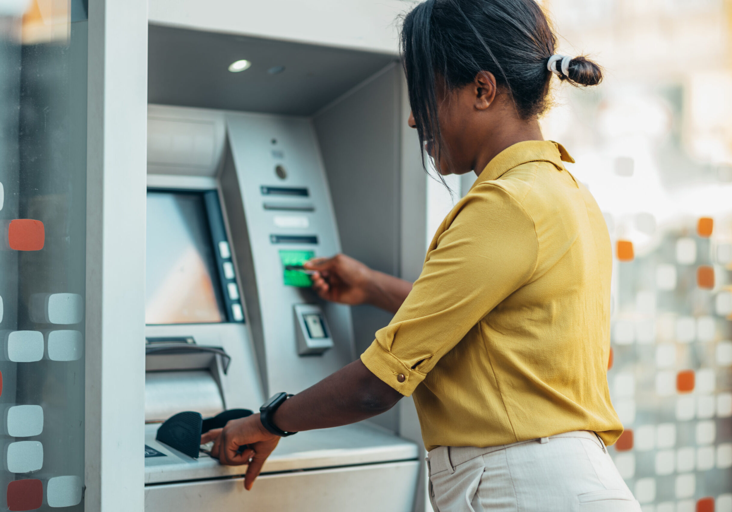 Beautiful young african american woman using an atm machine and a credit card while in the city