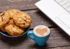 cookie and cup of coffee with laptop on wooden table.